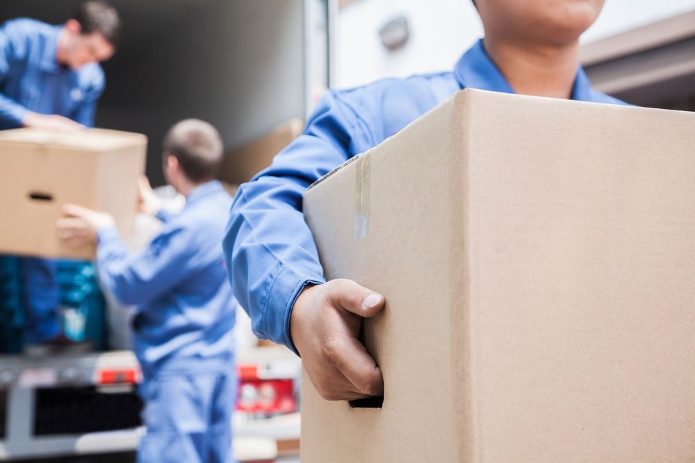 A man is carrying a cardboard box in front of a truck.