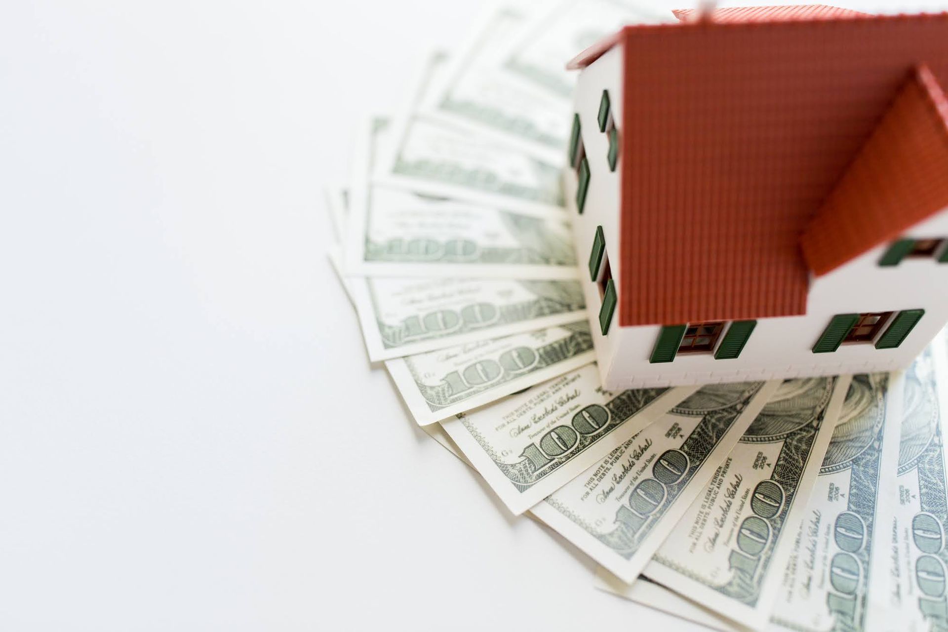 A model house is sitting on top of a pile of money.