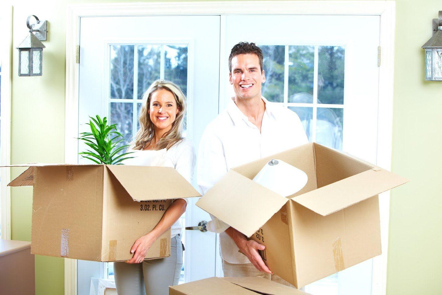 A man and a woman are holding cardboard boxes in a living room.