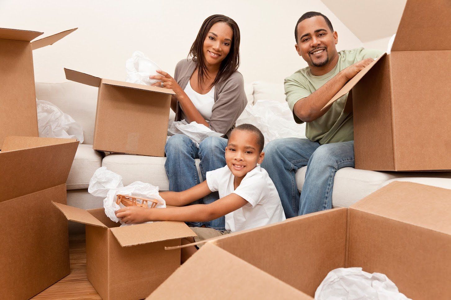 A family is sitting on a couch surrounded by cardboard boxes.