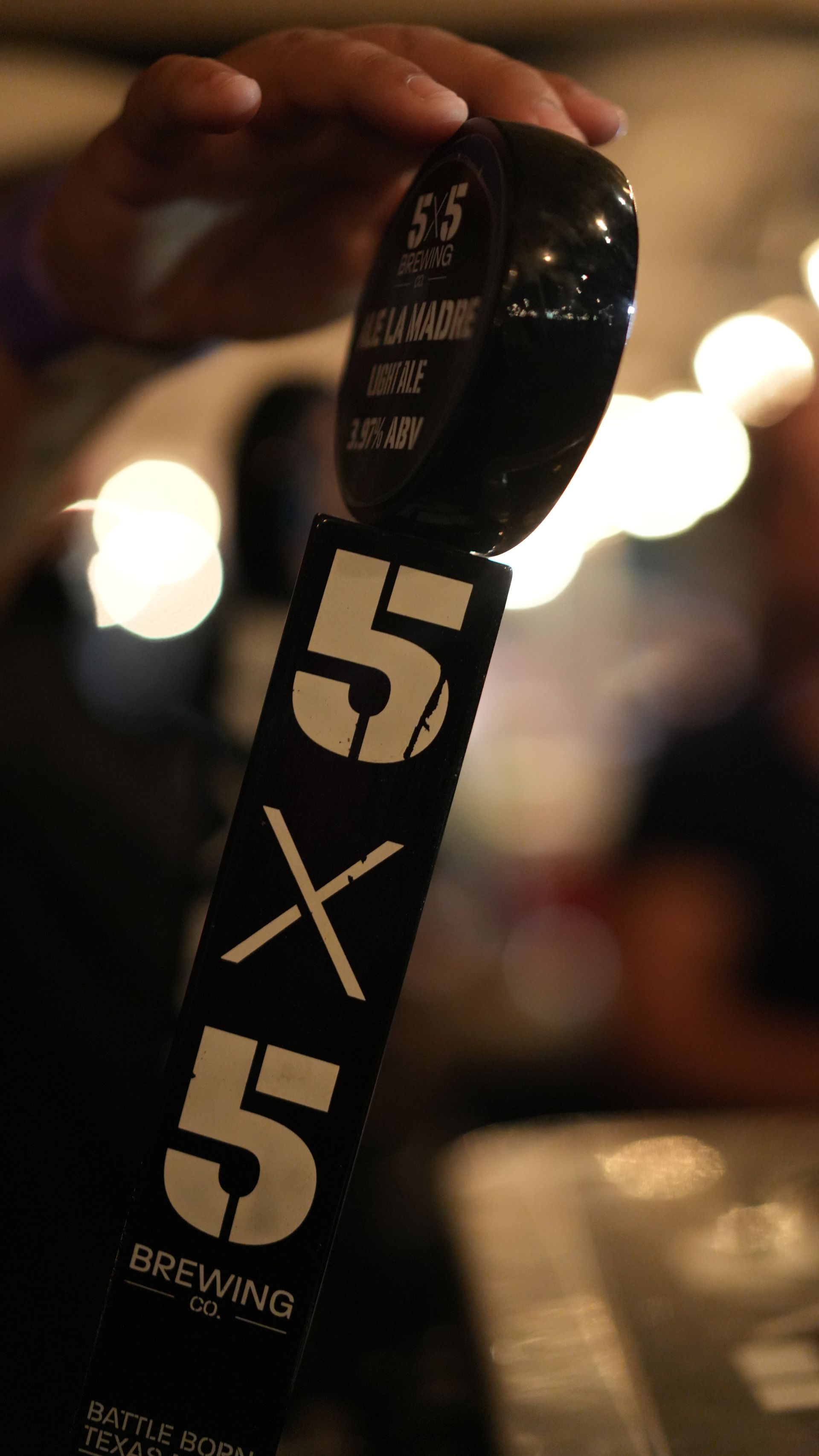 A person is holding a beer tap that says 5x5 on it.