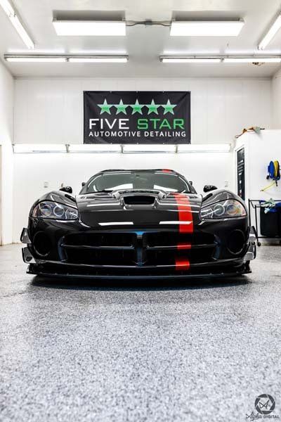 A black dodge viper is parked in a garage under a five star automotive detailing banner.