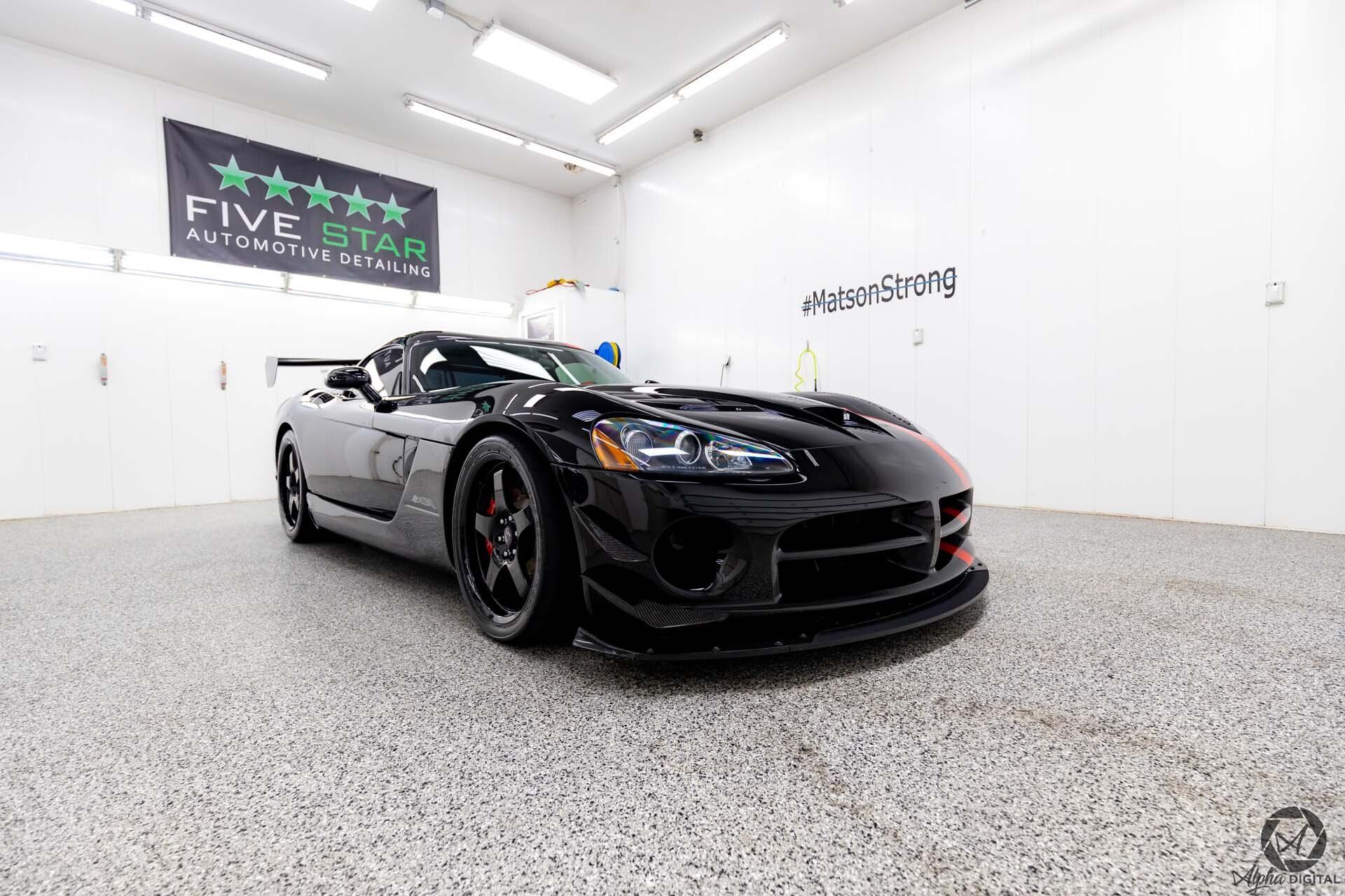 A black sports car is parked in a garage next to a sign that says five star.