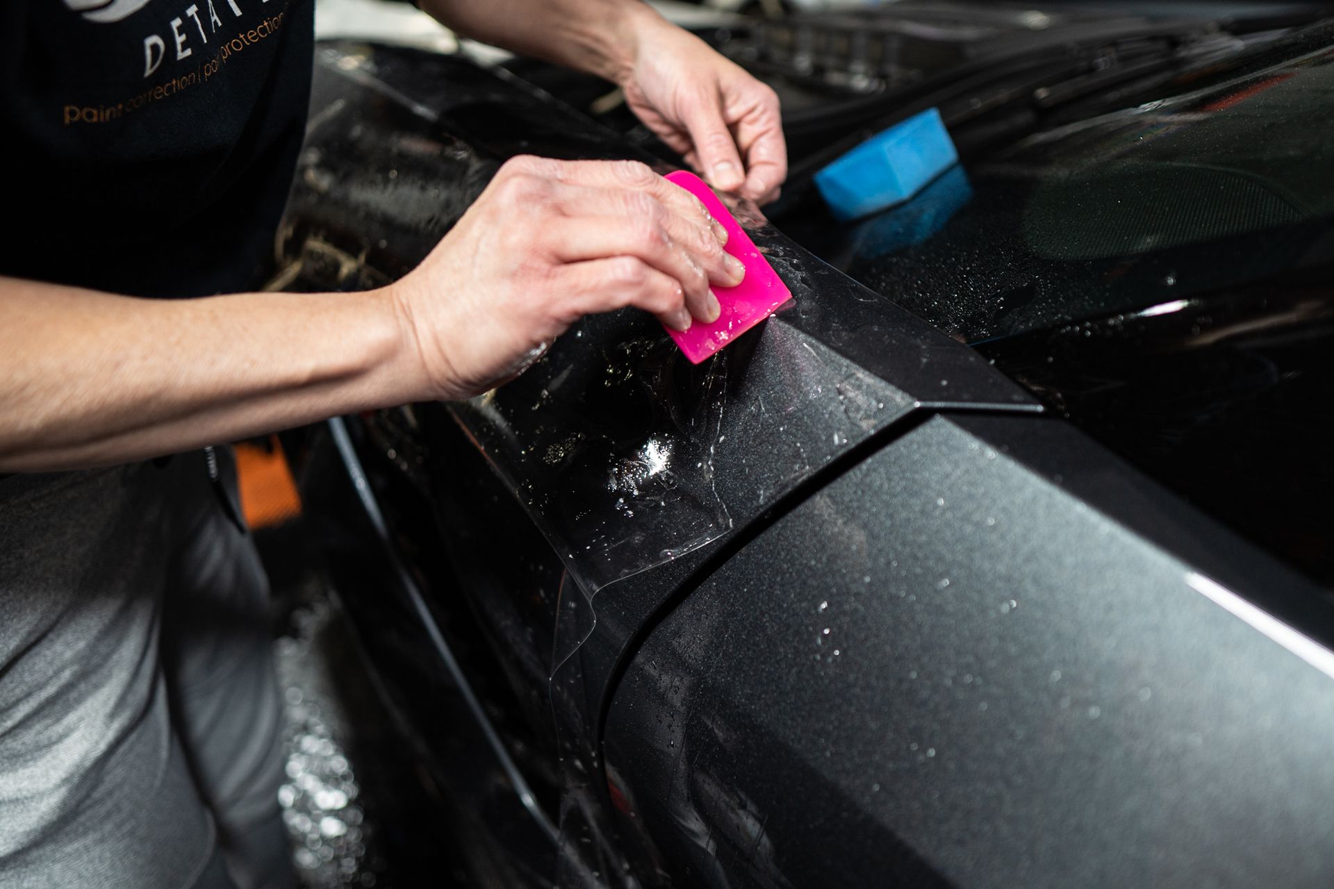 A person is applying a protective film to the hood of a car.