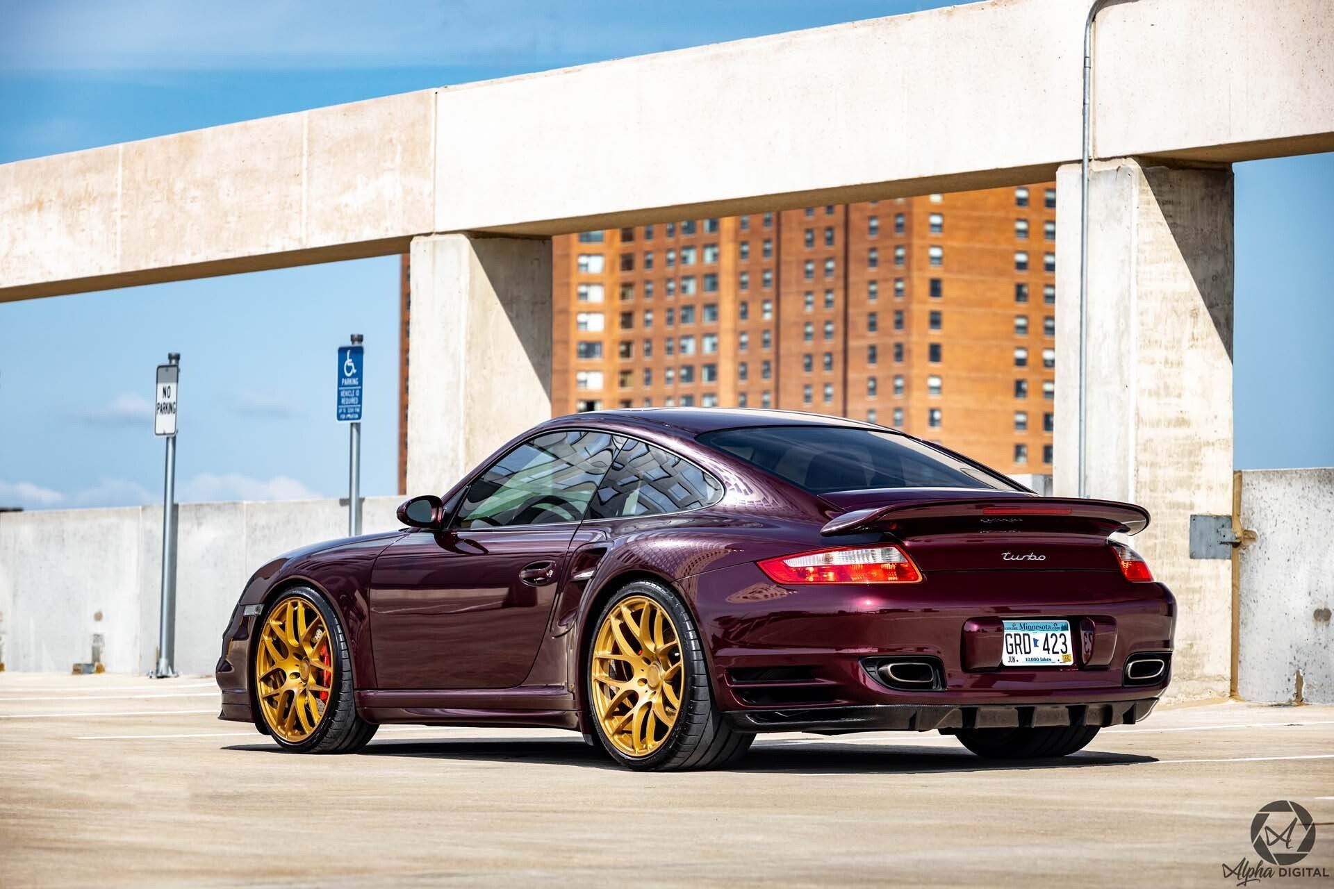 A purple porsche turbo is parked in a parking lot in front of a building.