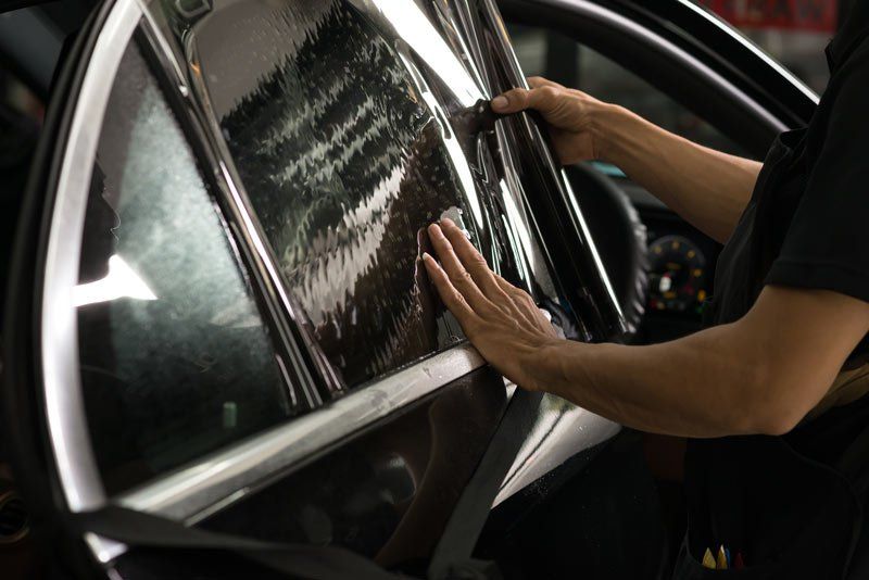 A man is applying tinted window film to a car window.