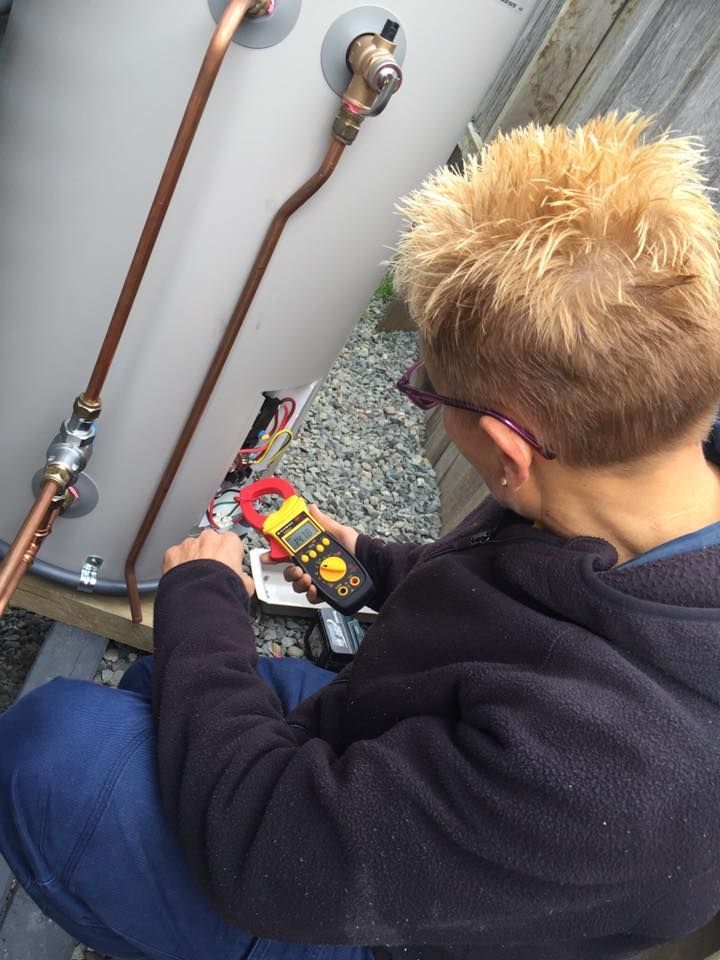 A Woman is Working on a Water Heater With a Clamp Meter — Dylko Electrical in Wauchope, NSW