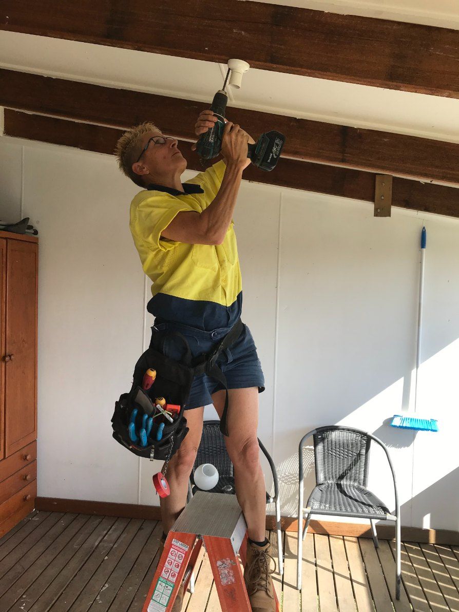 A Man is Standing on a Ladder Working on a Light Fixture — Dylko Electrical in Wauchope, NSW
