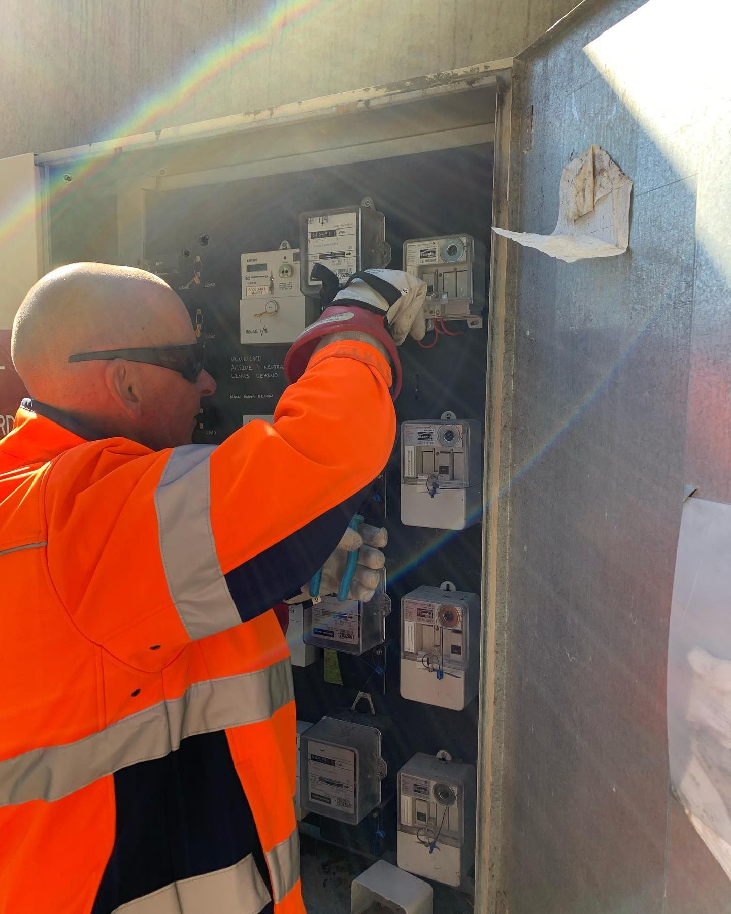 A Man in an Orange Jacket is Working on an Electrical Box — Dylko Electrical in Wauchope, NSW