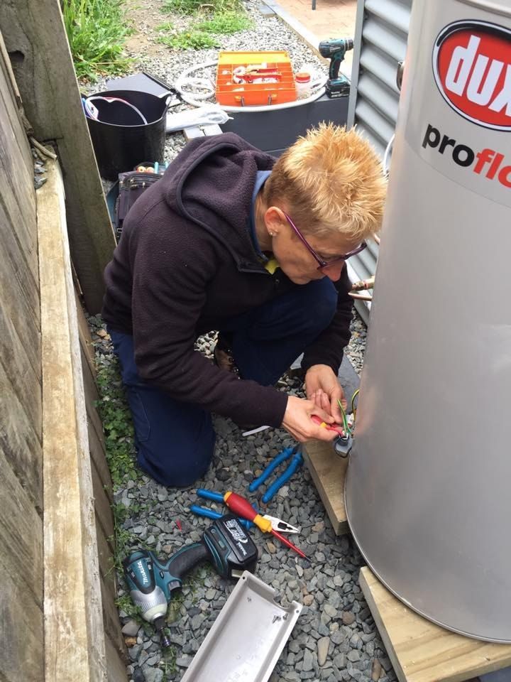 A Man is Working on a Water Heater Outside — Dylko Electrical in Wauchope, NSW