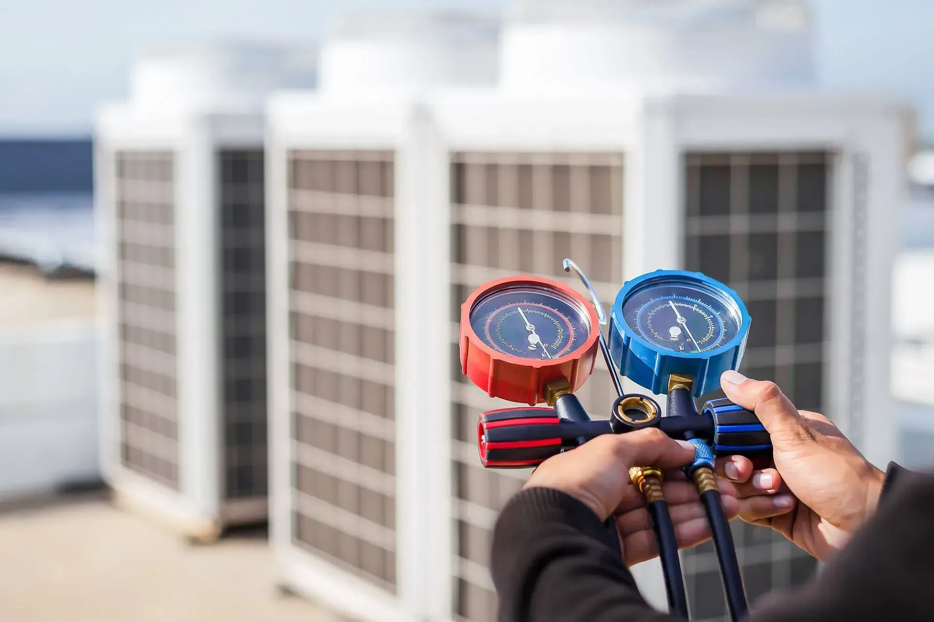 A person is holding a pressure gauge in front of a row of air conditioners.