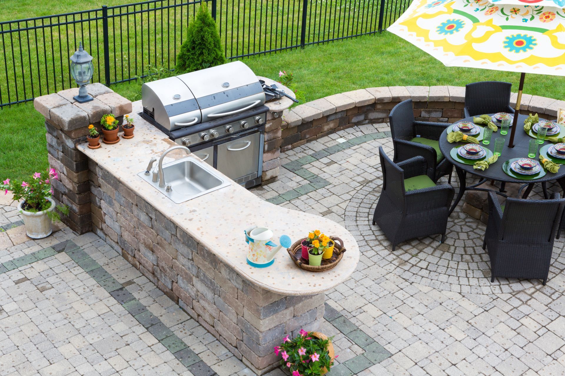 A patio with a grill , table and chairs and an umbrella.