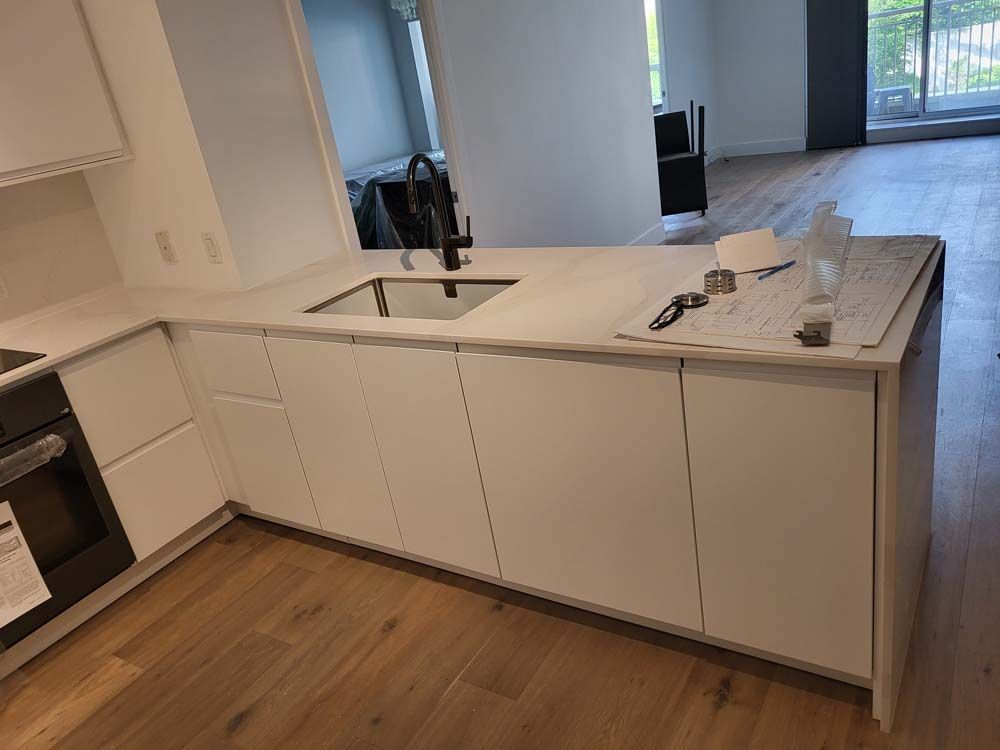 A kitchen with white cabinets , a sink , and a wooden floor.