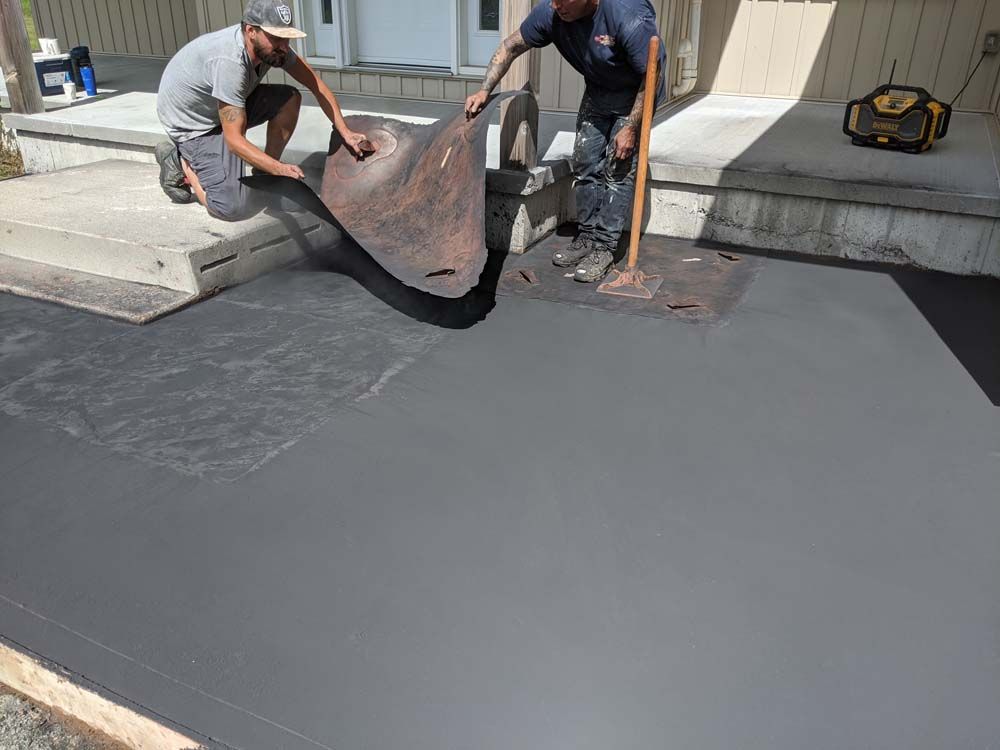 Two men are working on a concrete driveway.