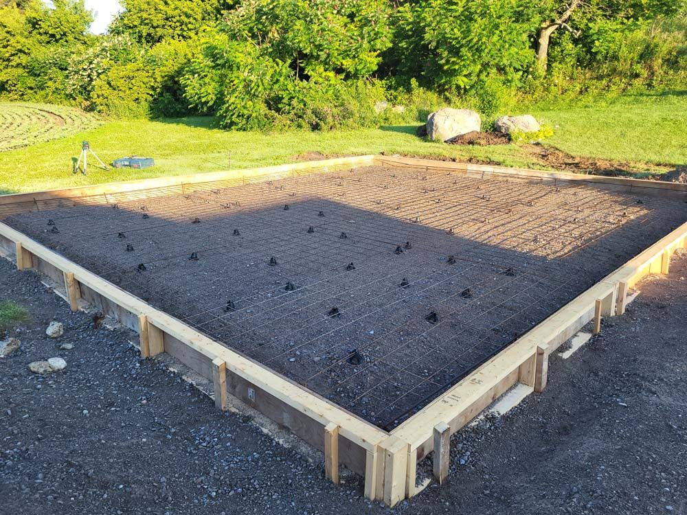 A concrete foundation is being built in a yard with trees in the background.