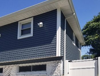 a house with a blue siding and white trim has a white fence in front of it .