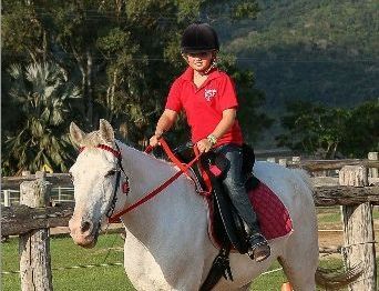 A Young Boy In A Red Shirt Is Riding A White Horse — Farleigh Saddle Club In Farleigh, QLD
