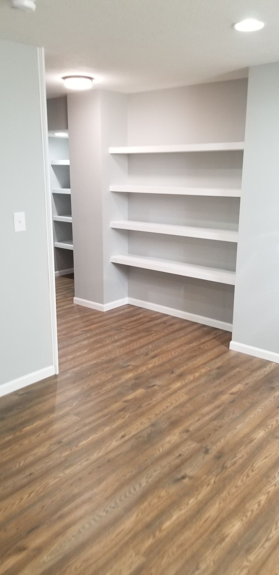 An empty room with wooden floors and white shelves.