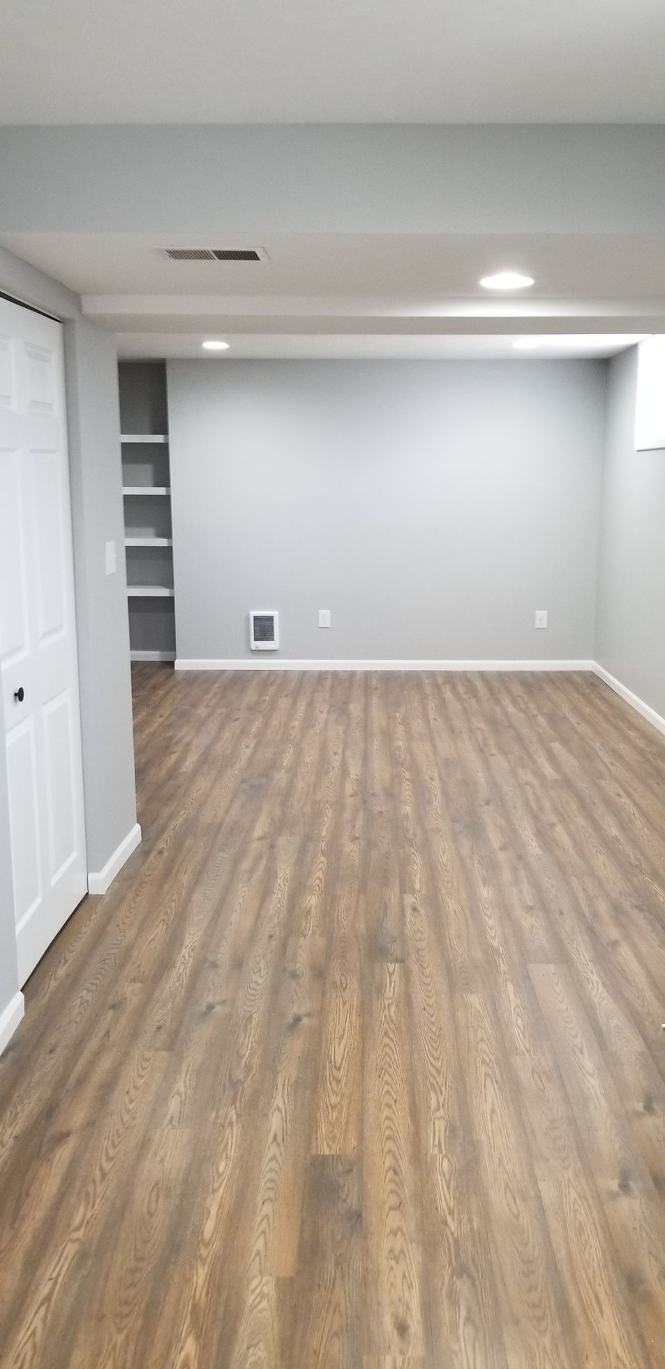 An empty basement with hardwood floors and gray walls.