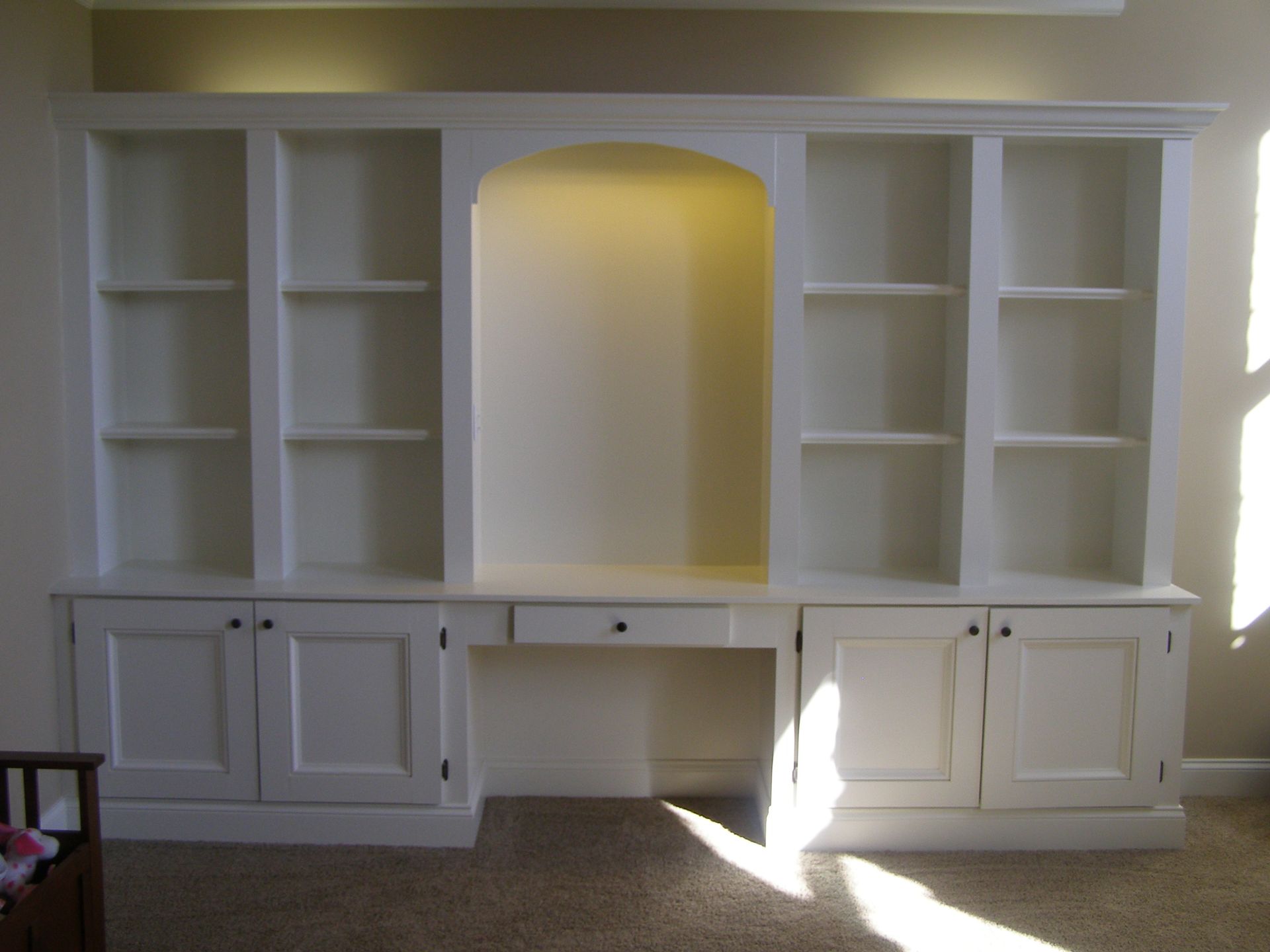 A room with white cabinets and shelves and a desk