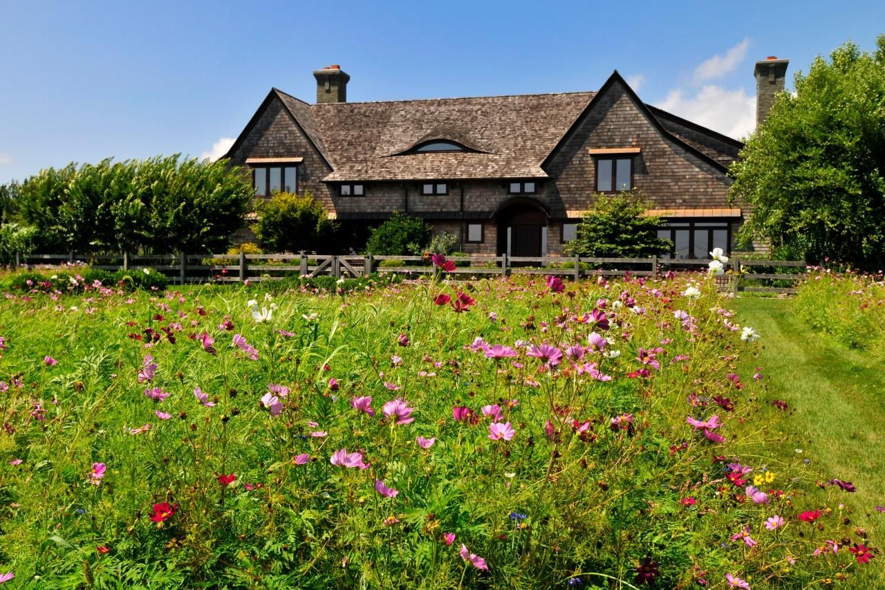 A large house is surrounded by a lush green field of flowers