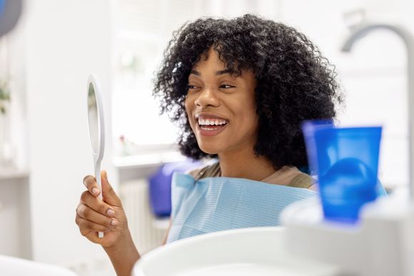 A woman is smiling while looking at her teeth in a mirror.