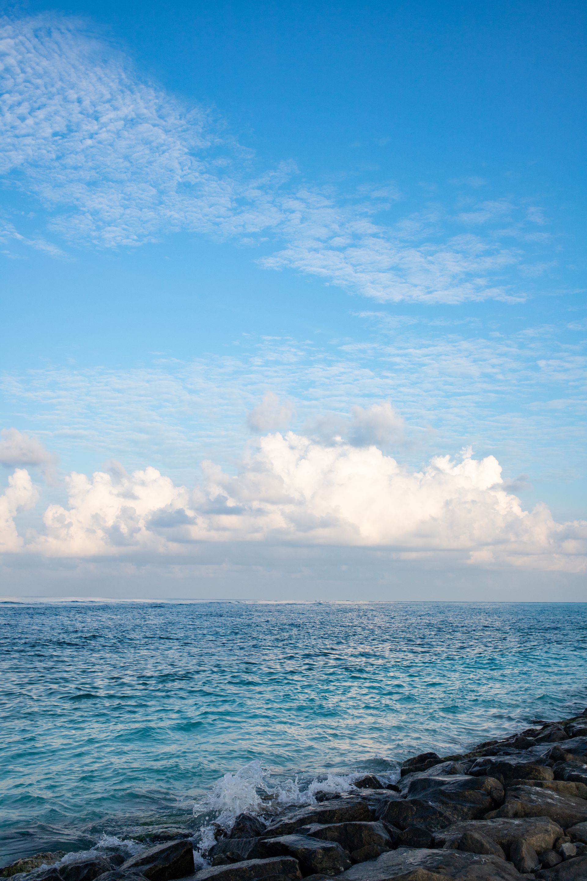 Ocean with blue water, white clouds, and a rocky shoreline under a bright sky.
