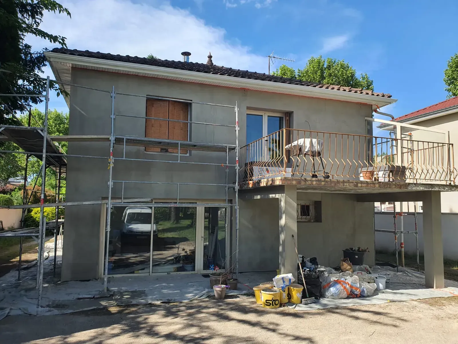 Une maison à deux étages en rénovation, avec des échafaudages, un balcon avec des rambardes métalliques et du matériel de construction.