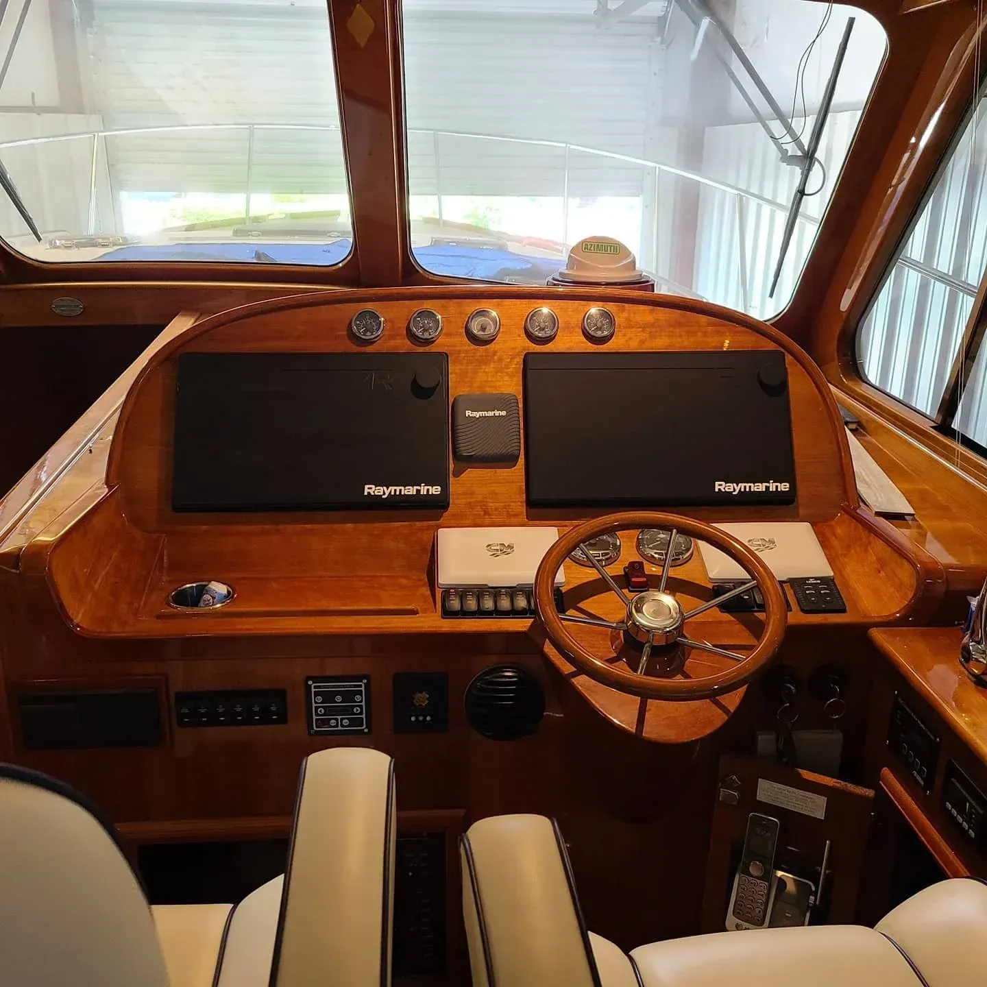 Boat cockpit with wooden dashboard, dual screens, and steering wheel.