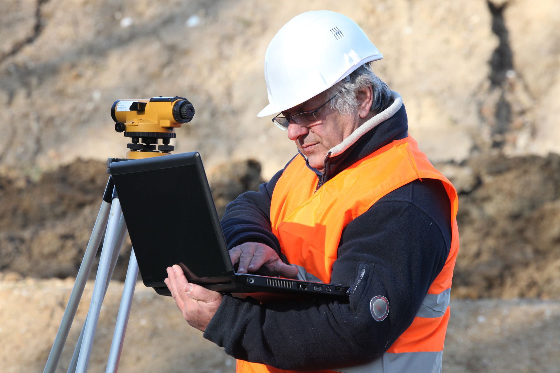 A surveyor outdoors working with a laptop and conducting a survey.