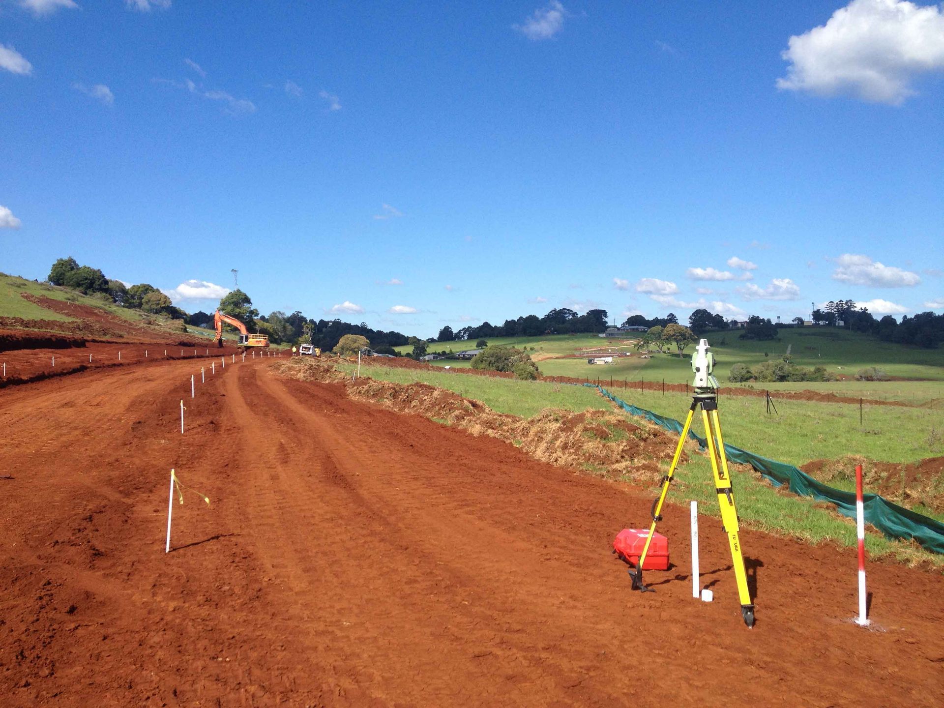 Surveying equipment on a red dirt road under a blue sky at a construction site.