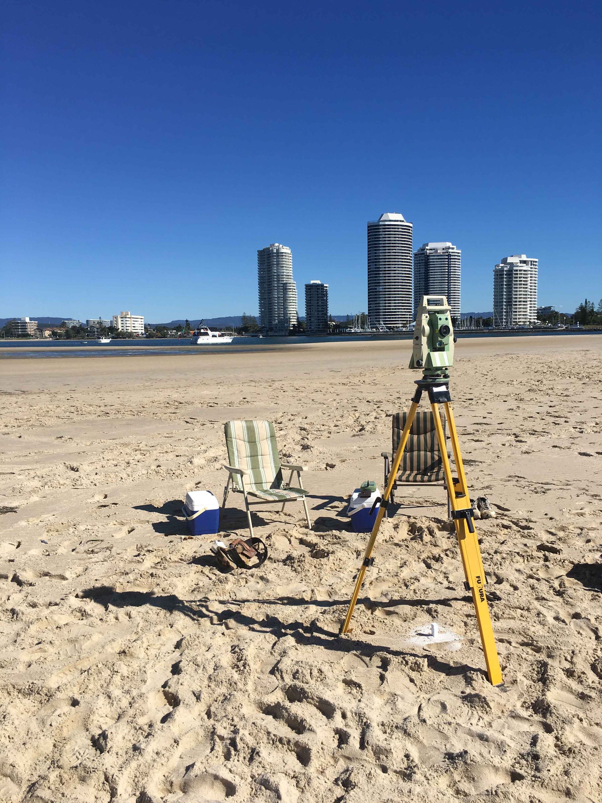 Survey equipment on a beach, with city skyscrapers in the background on a sunny day.