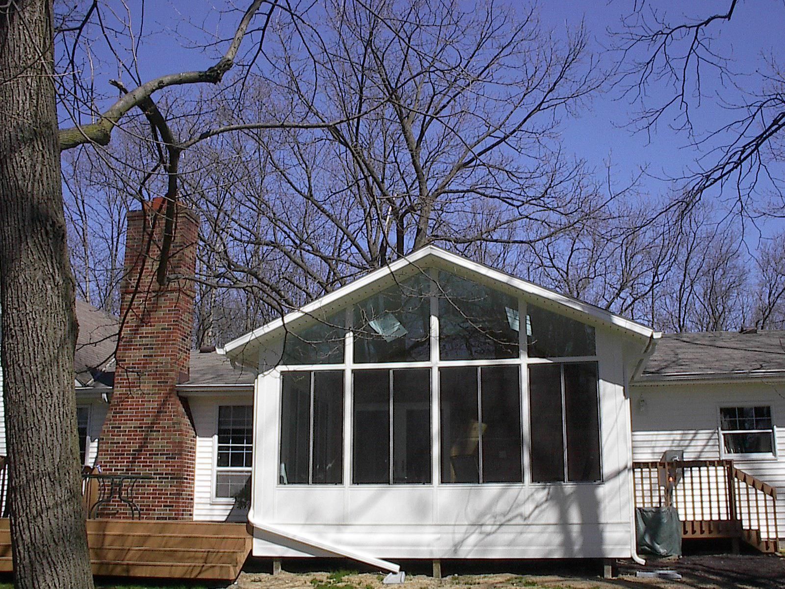 A white house with a screened in porch and a brick chimney