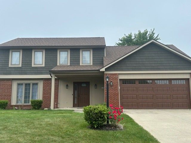 Two-story house with green siding, brown roof, red brick accents, and a brown garage door.