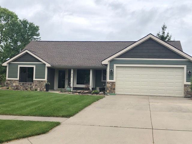 Green ranch-style house with stone accents, a beige garage door, and a brown roof under a cloudy sky.