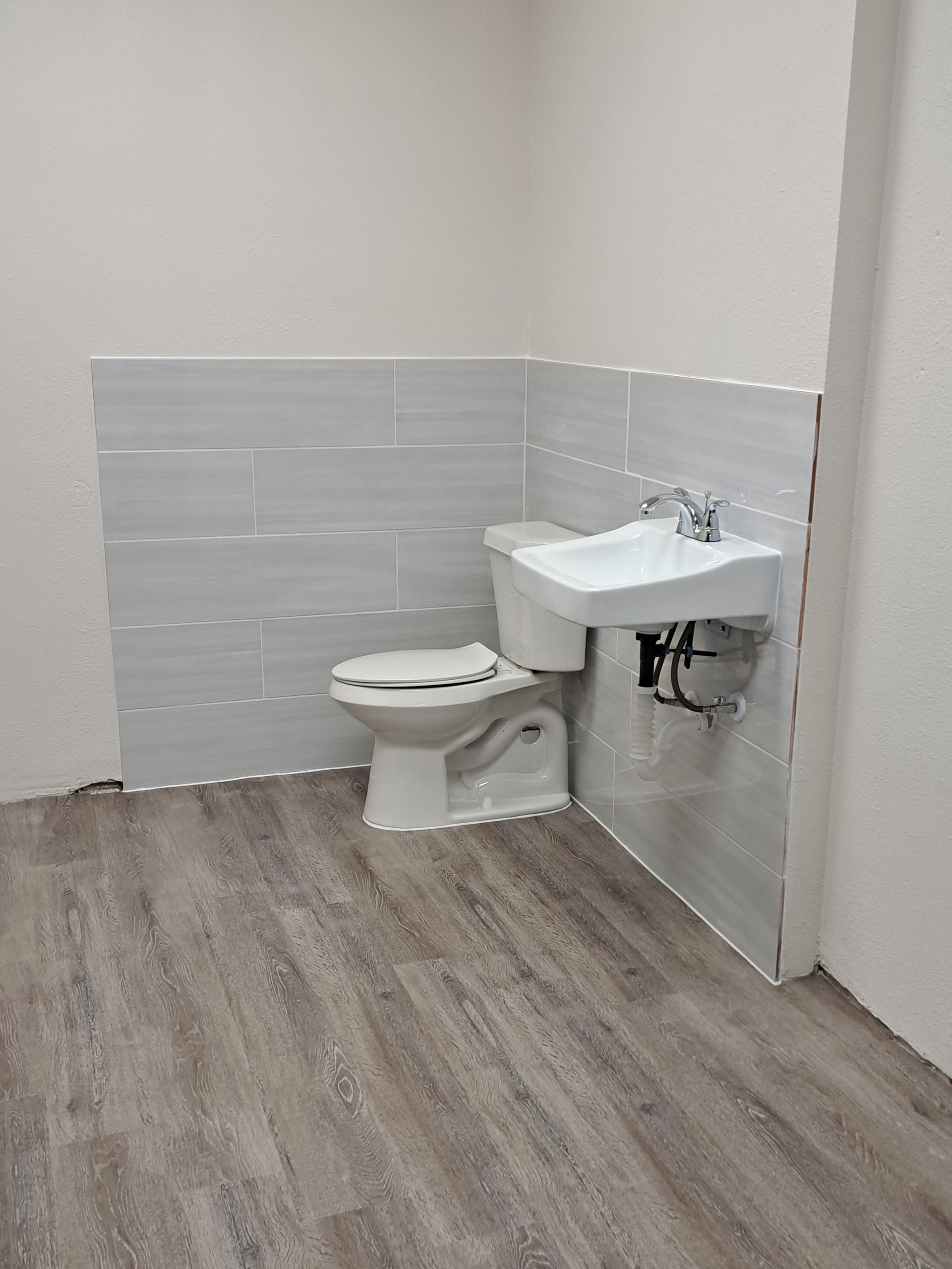 Bathroom with toilet and sink against tiled wall; wood-look flooring.