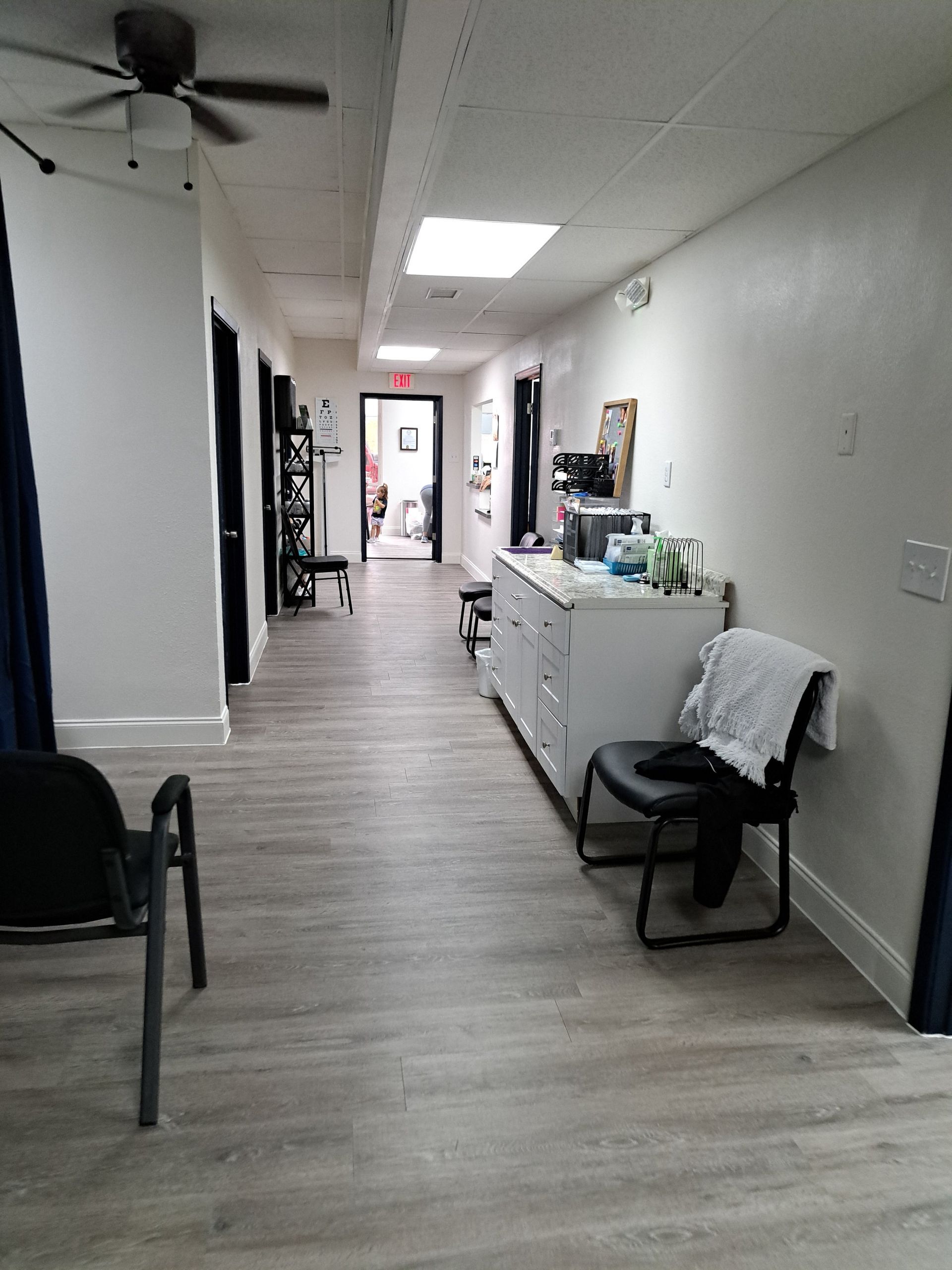 Long hallway with light wood-look flooring, white walls, and black doors. A ceiling light and a small office area are visible.
