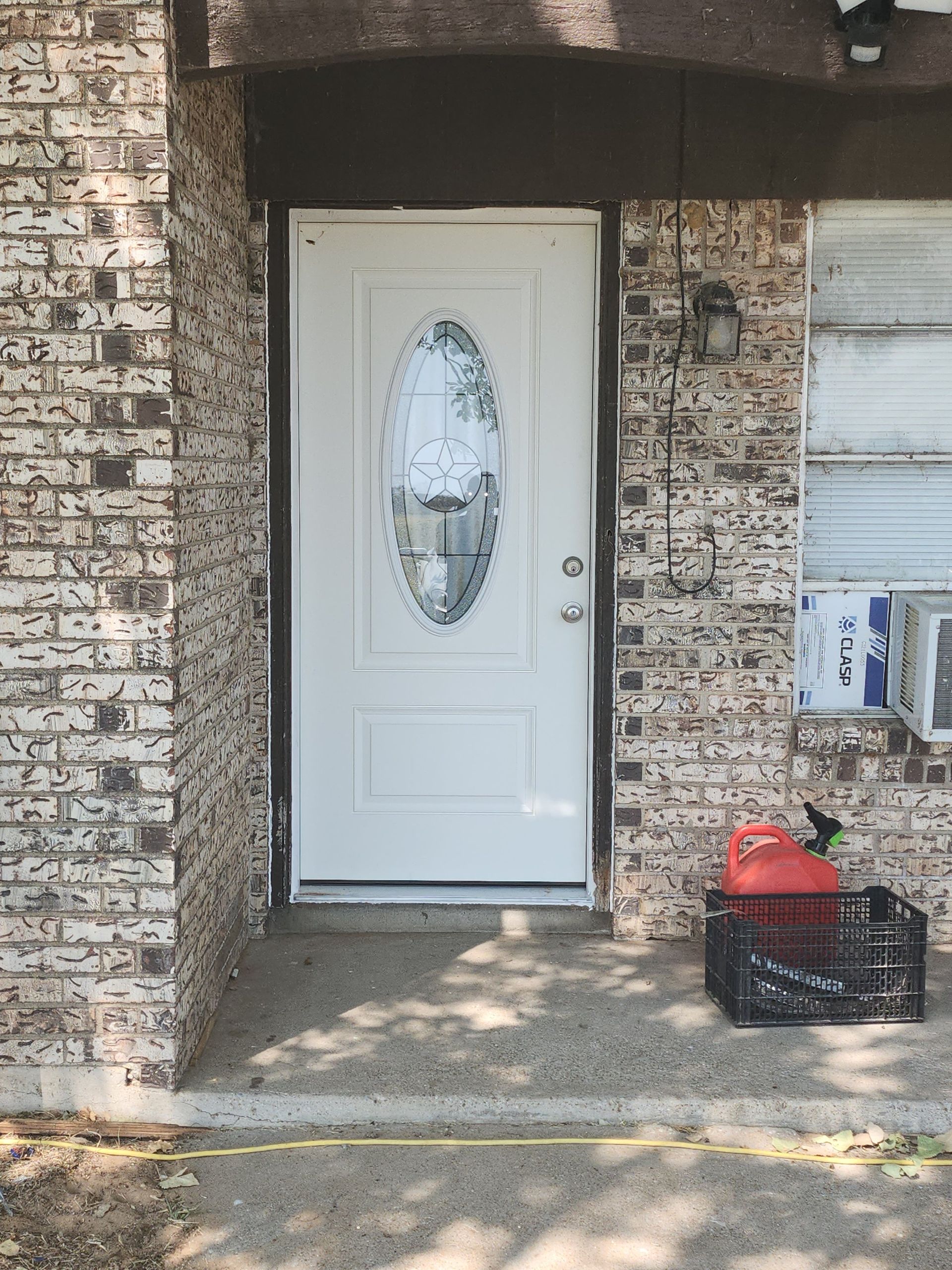 White front door with oval glass, brick exterior, and a black crate on the porch.