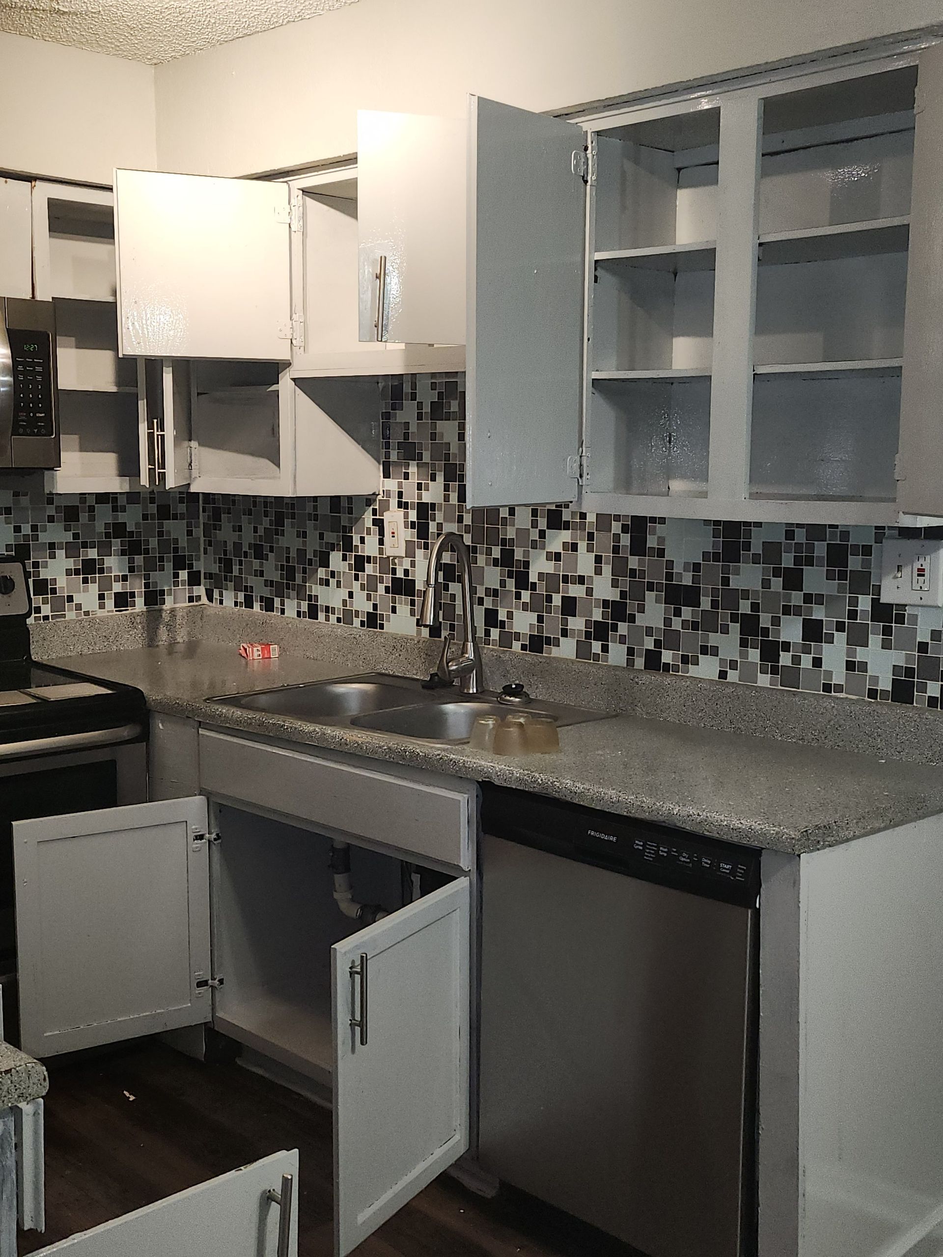 Kitchen with gray cabinets, granite countertops, and black and white backsplash; cabinets are open.