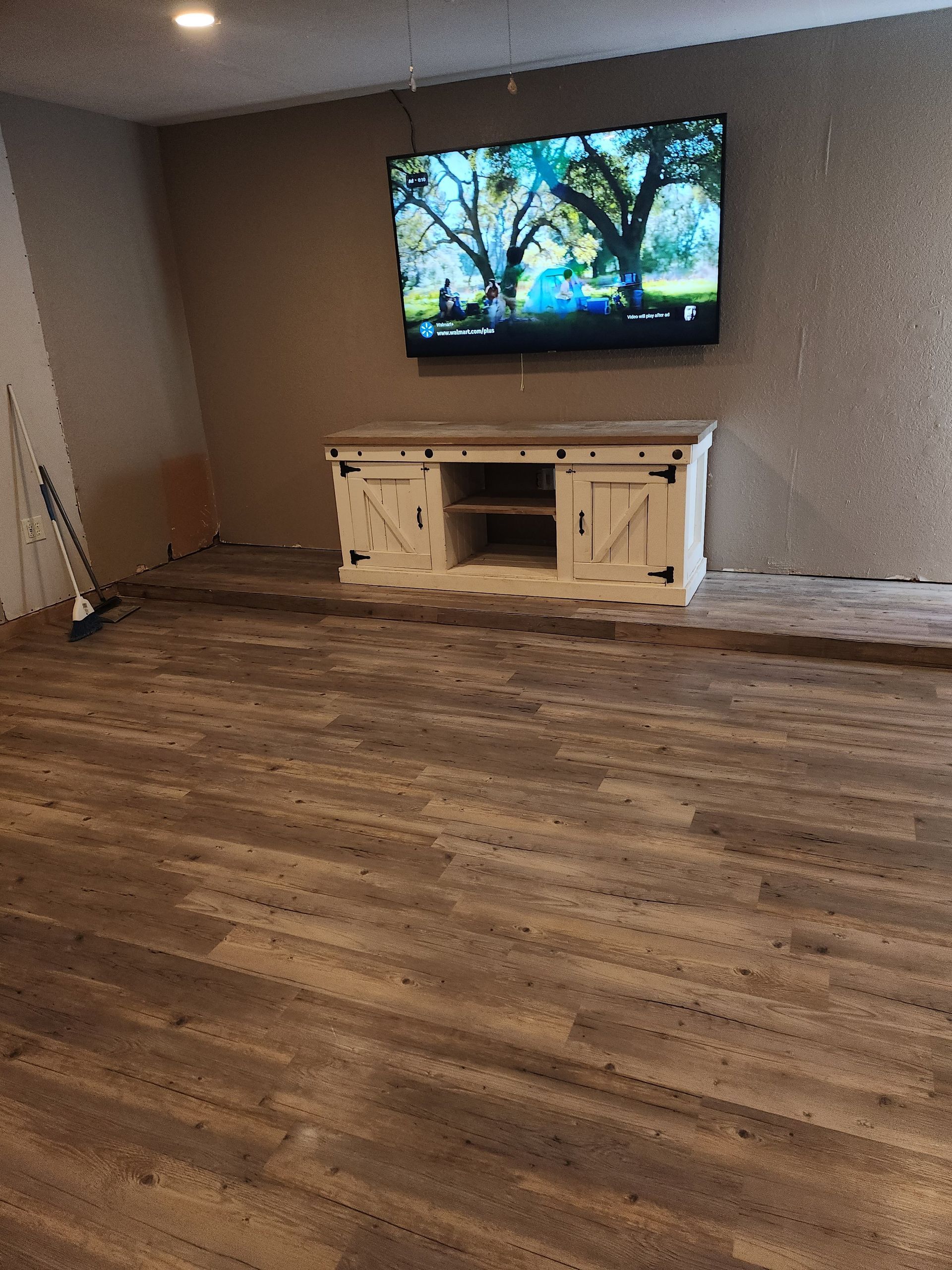 Wooden-floored room with a mounted TV above a white cabinet. The wall is textured and beige.