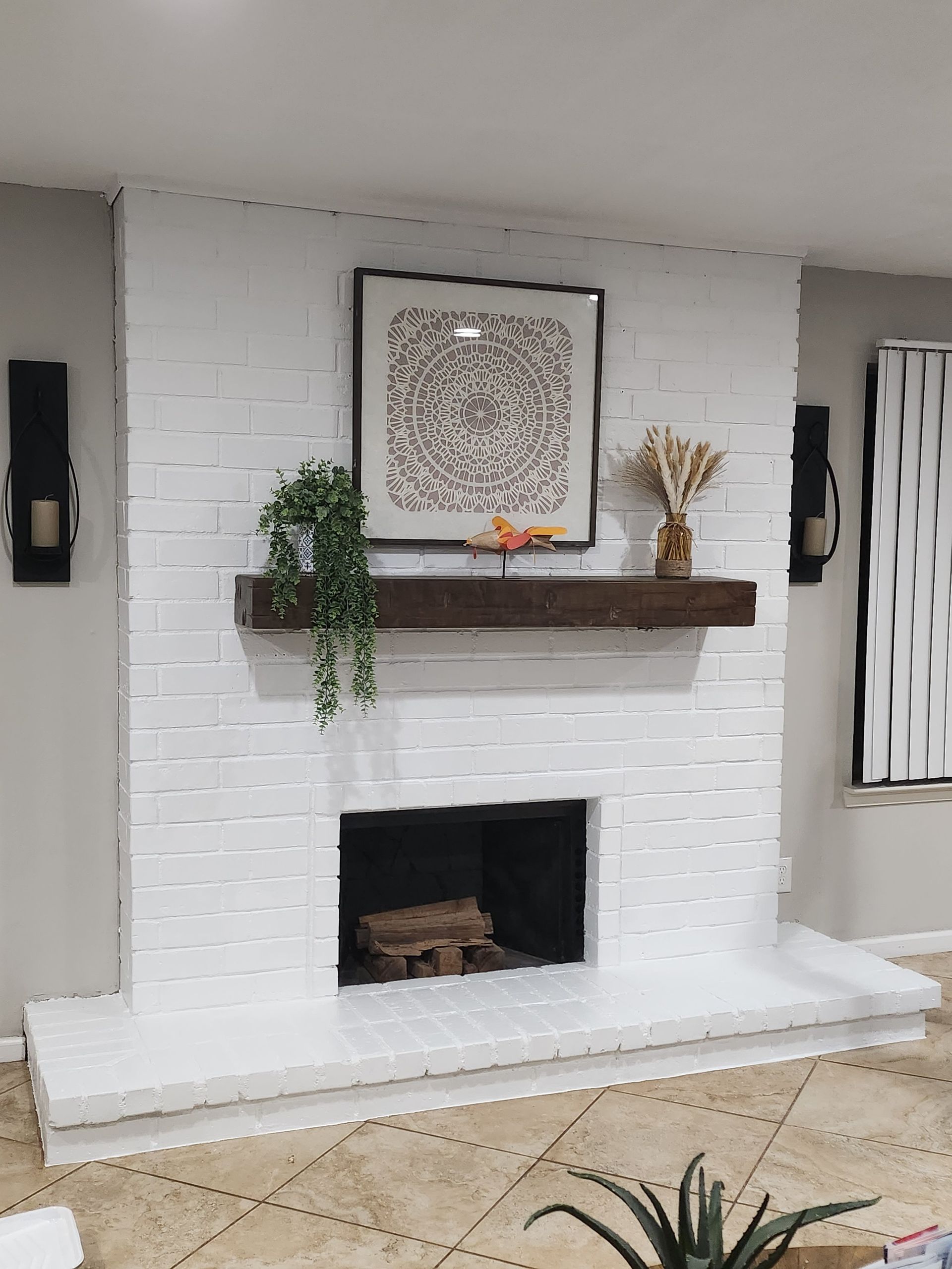 White brick fireplace with dark wood mantel and artwork, flanked by sconces.
