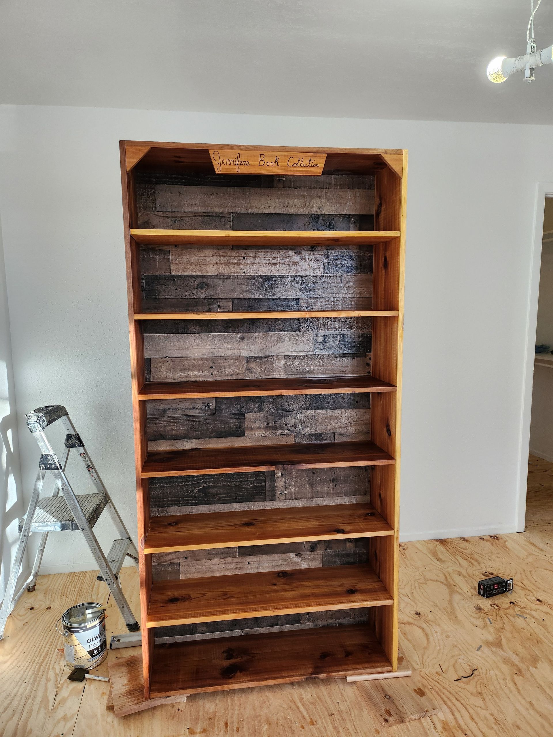 Tall wooden bookshelf with rustic plank backing and shelves, against a white wall.