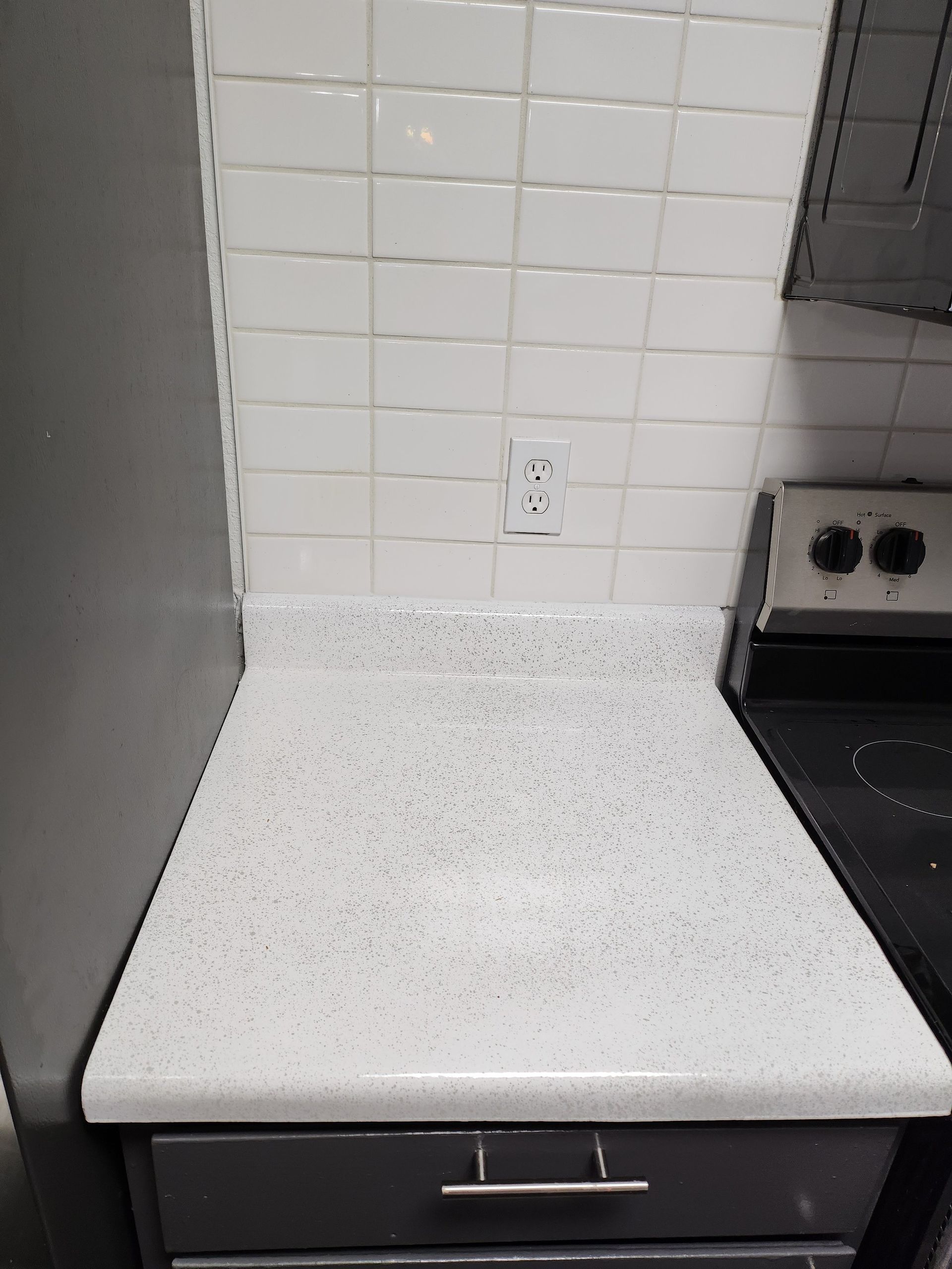 White speckled countertop with white subway tile backsplash, stove and cabinet.