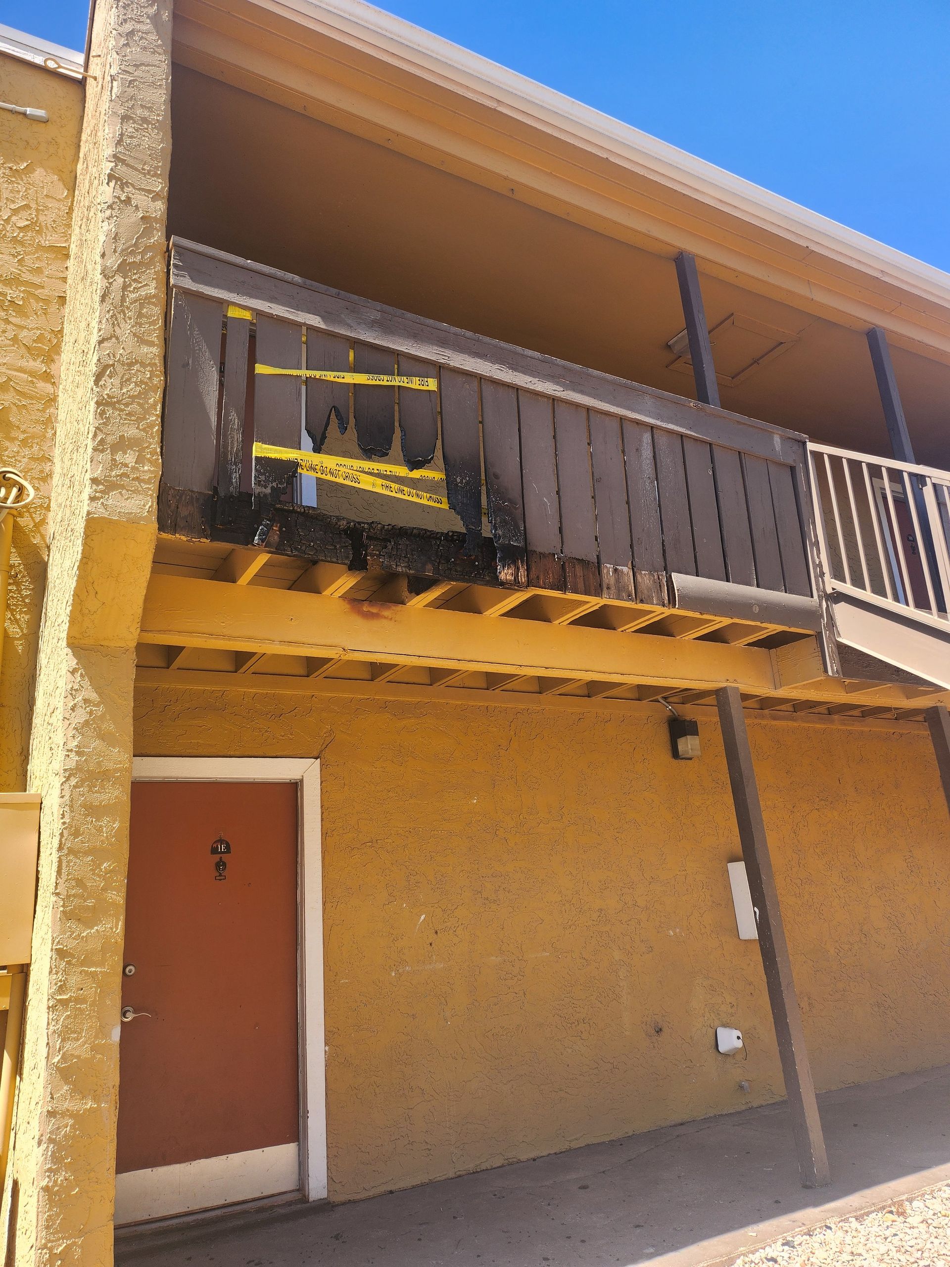 Building exterior with a second-story balcony sectioned off with yellow caution tape; doorway below.