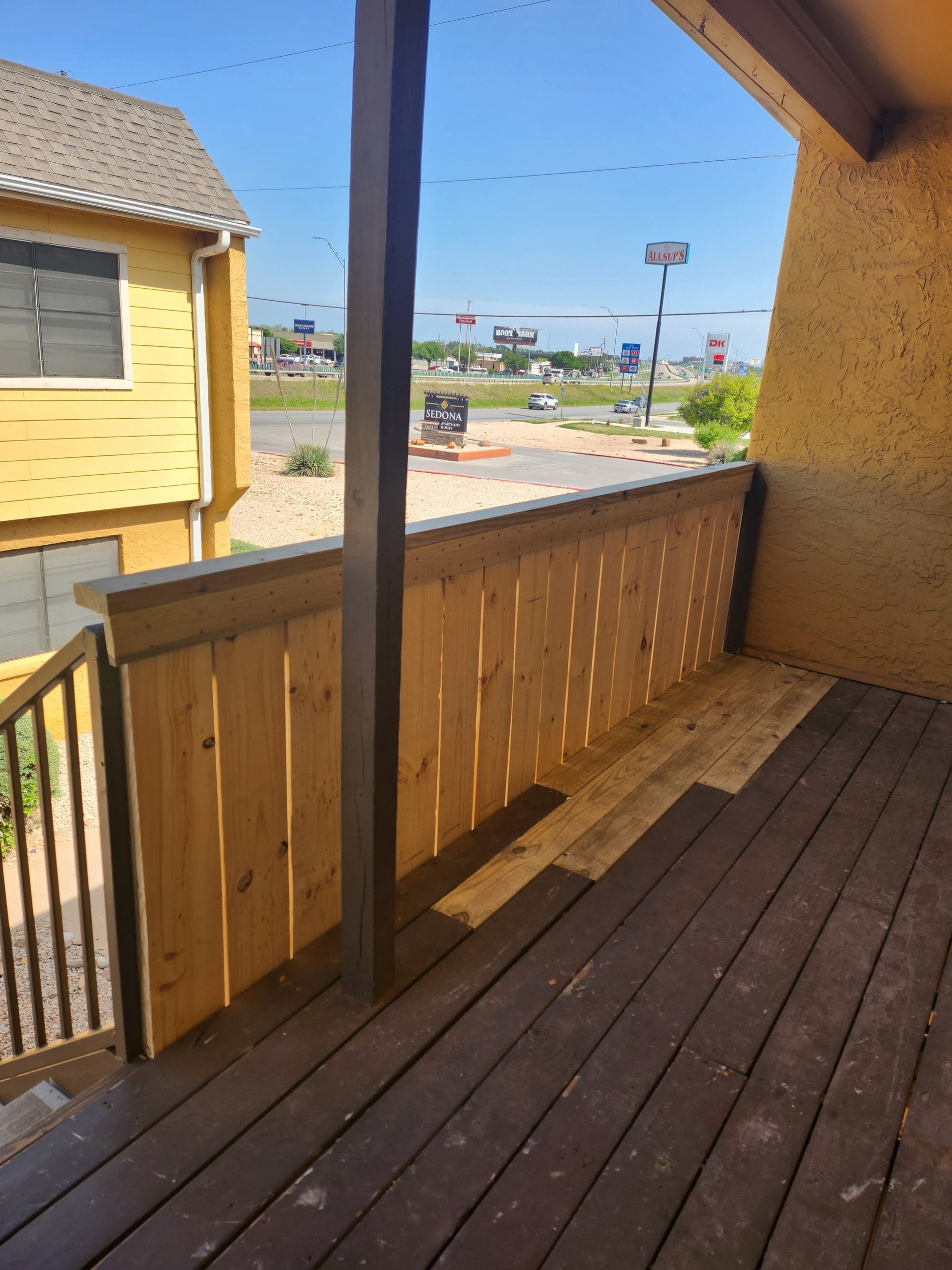 Wooden deck with a brown railing and a view of a street on a sunny day.