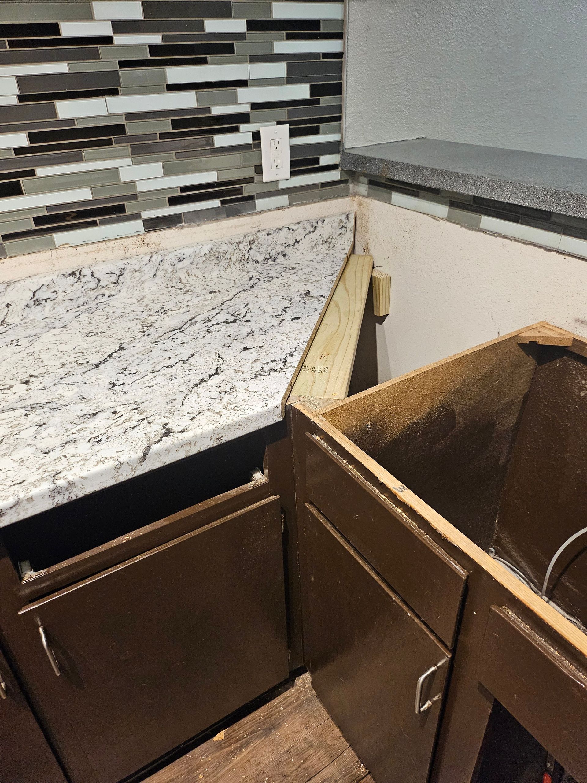 Kitchen countertop installation; granite countertops on brown cabinets, backsplash tile, sawdust present.