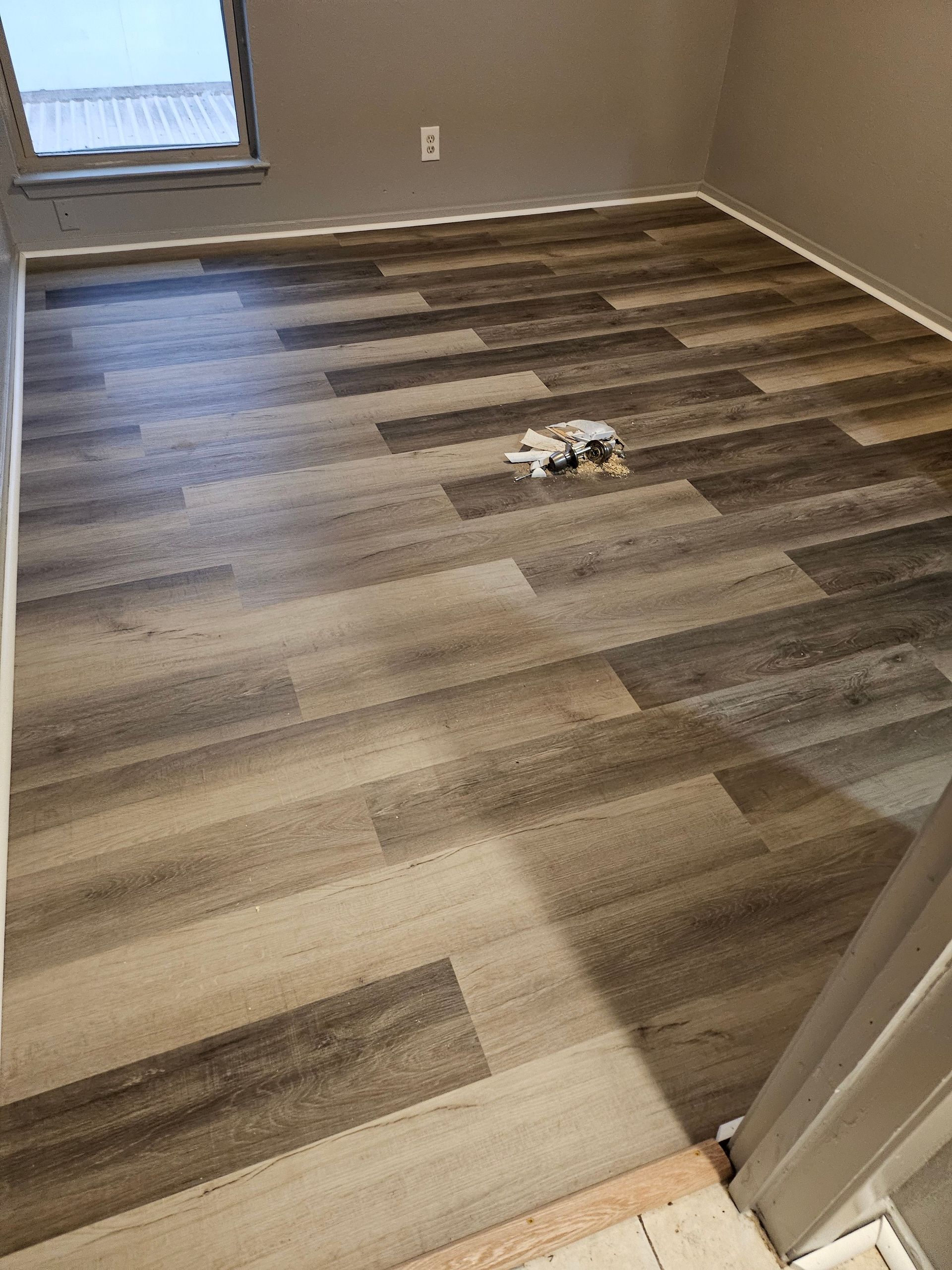 Room with new wood-look flooring. Light and dark brown planks, small window, white trim.