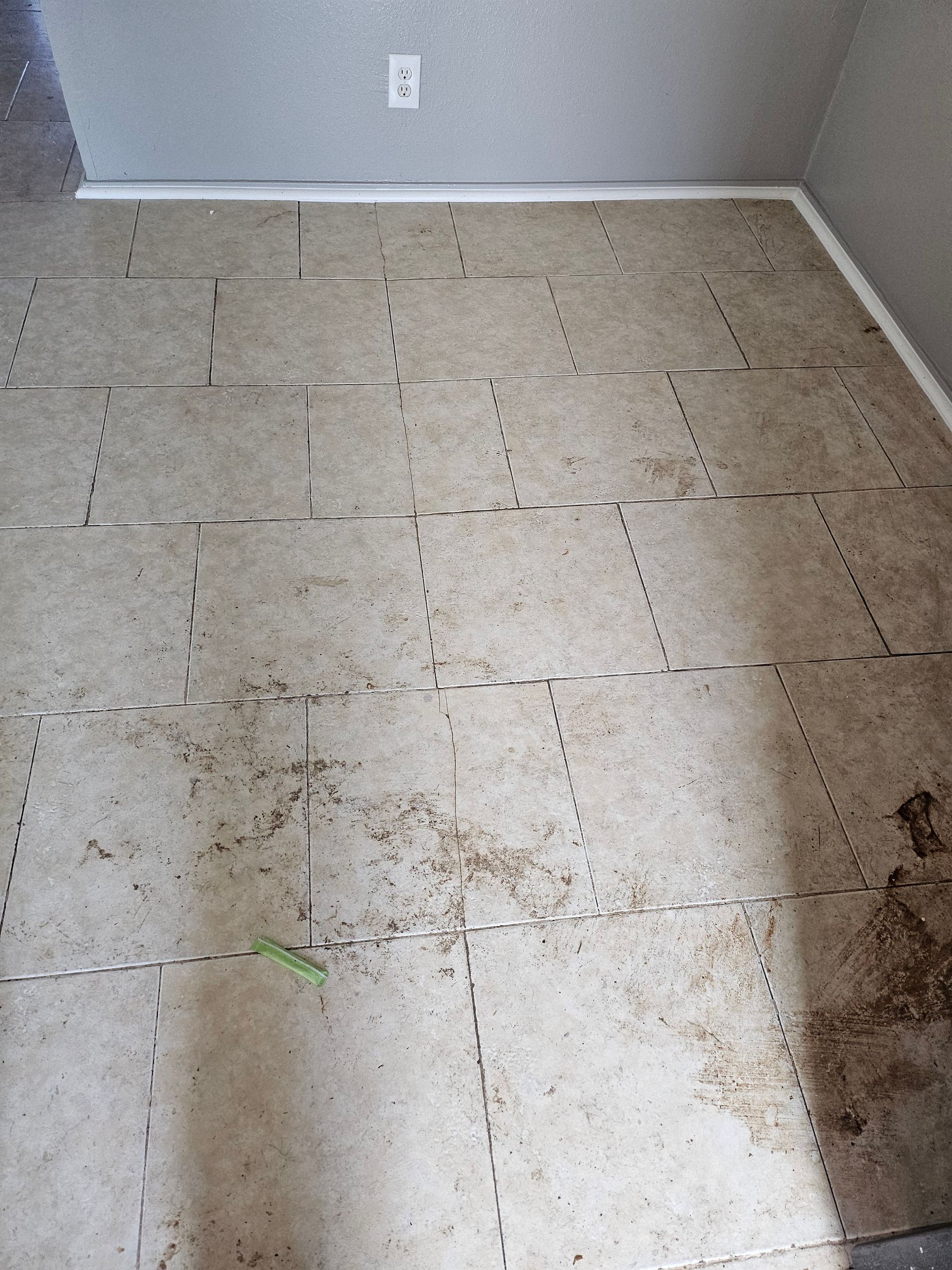Dirty, light-colored tile flooring, some sections separated. A wall with an electrical outlet is visible.