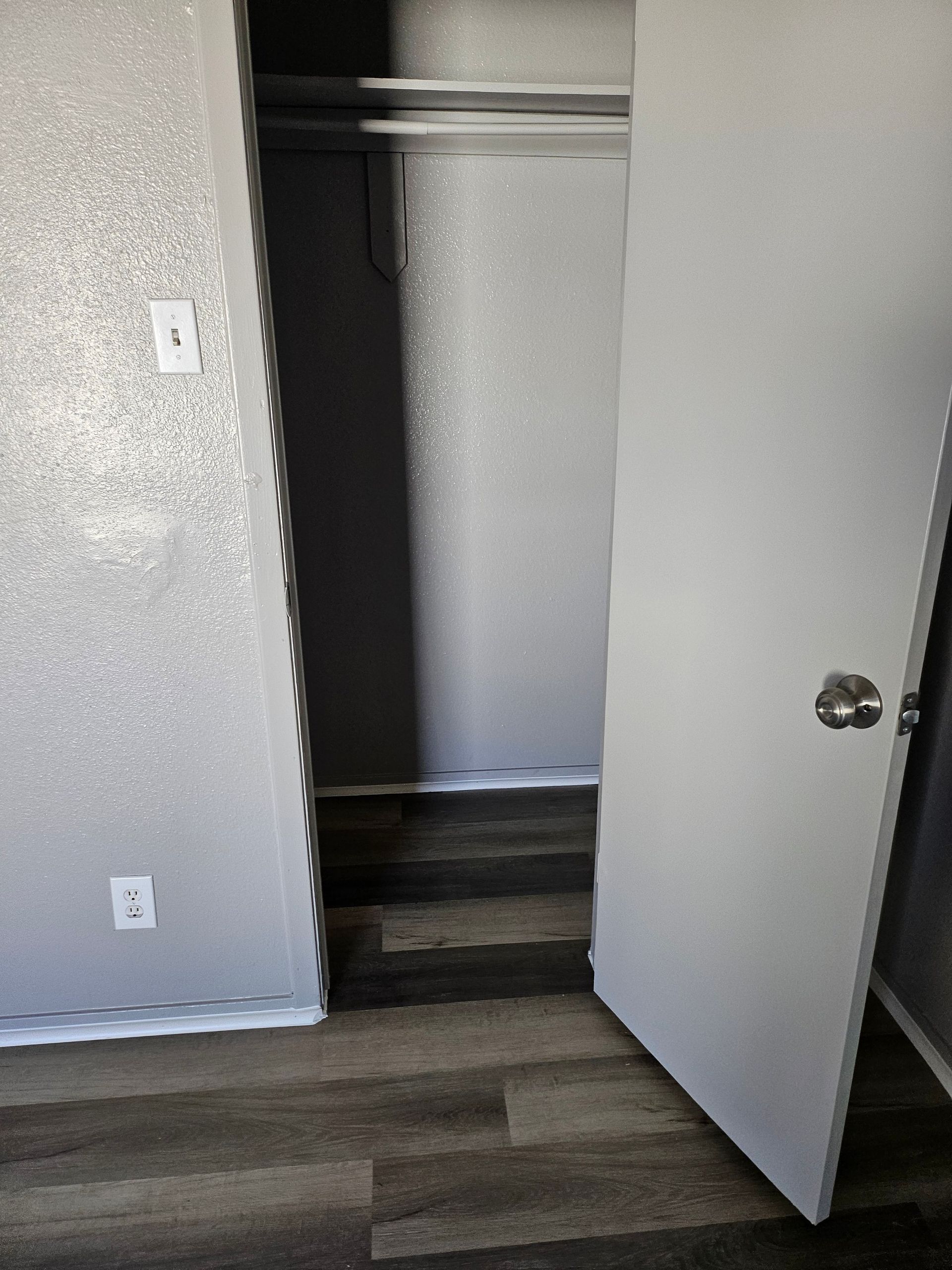 A doorway leads to a closet with a clothes rod. The door is slightly open, revealing wood-look flooring and gray walls.