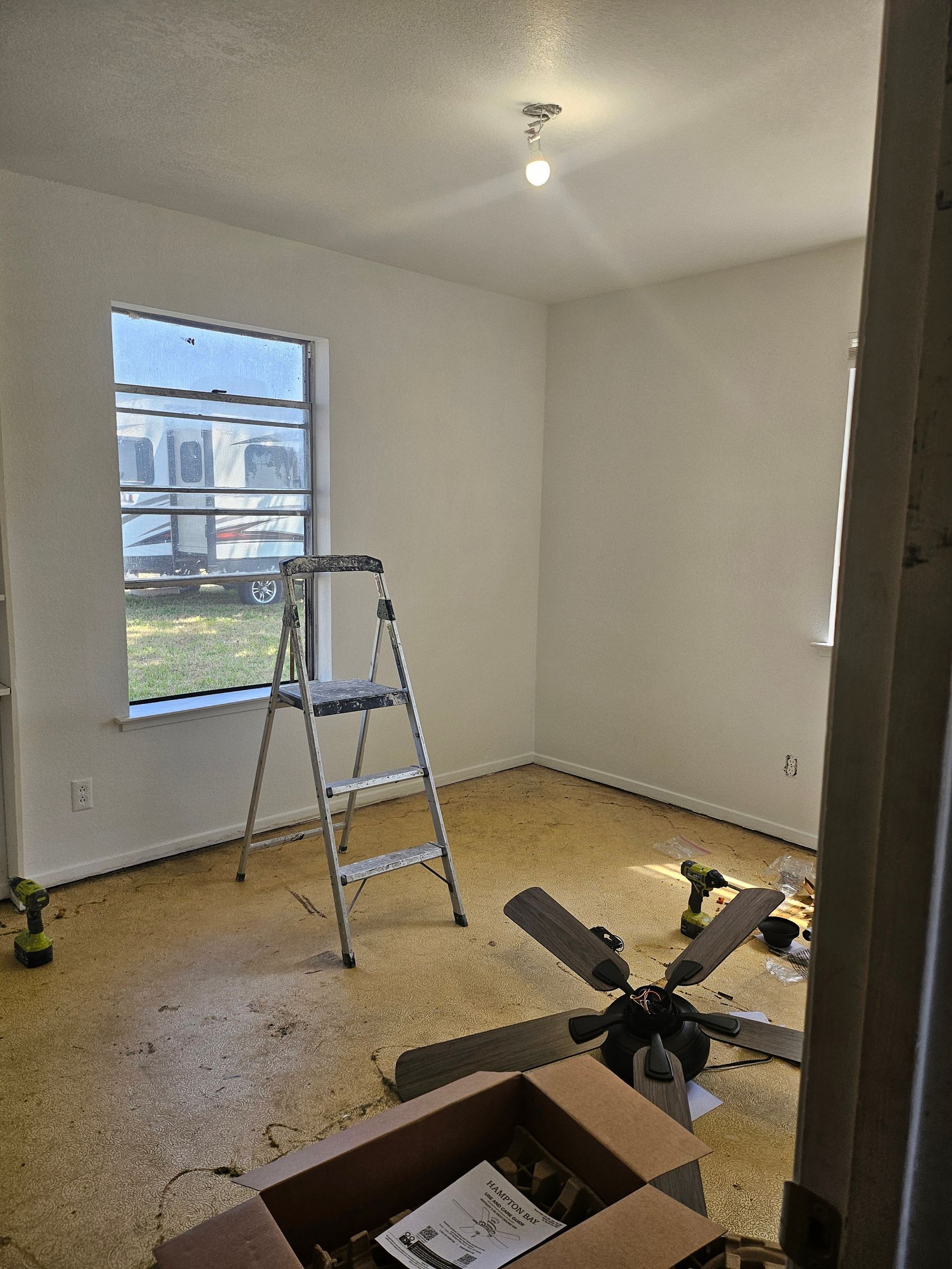 Room with unfinished renovations, ladder near window, ceiling fan on the floor.